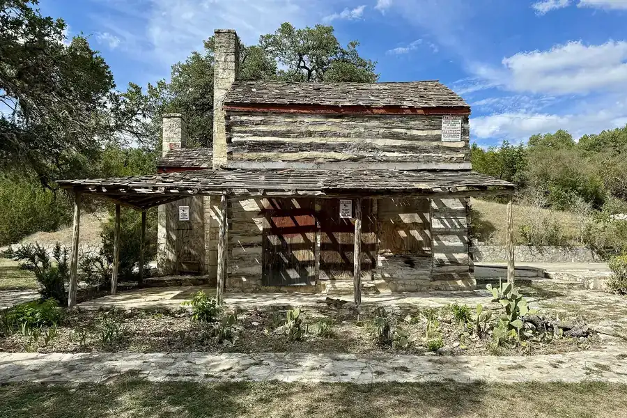 Historic John M. King Log House with a stone chimney among oak trees in Cedar Park, Texas