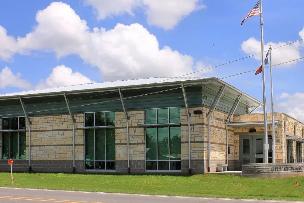 Manor city hall with a limestone and glass front and flags in Manor, Texas